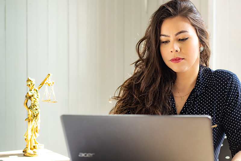 woman working on laptop beside statue of Lady Justice
