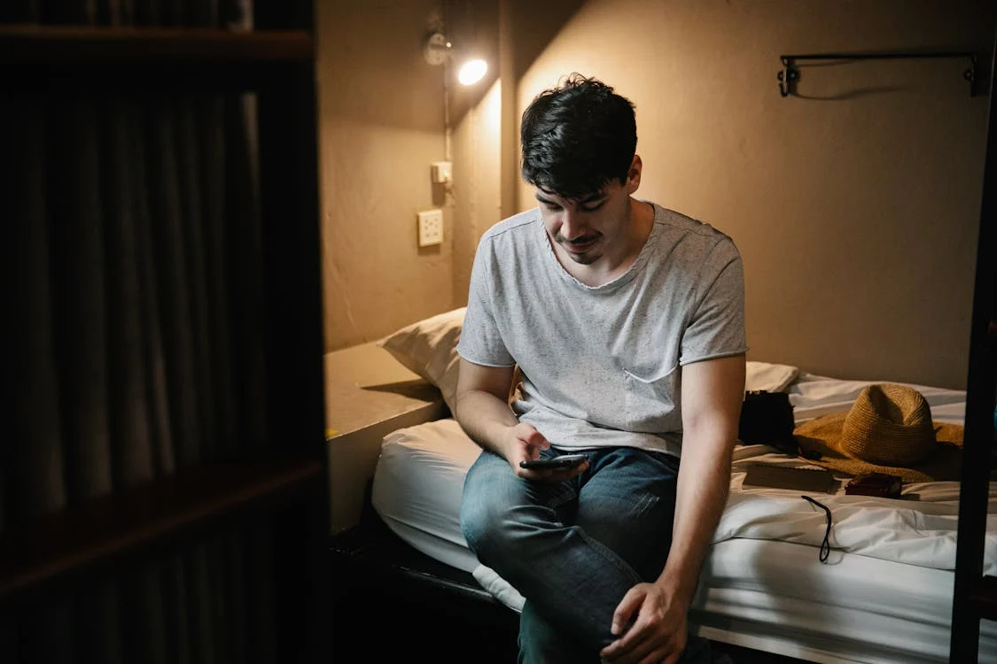 man sitting on bed using smartphone