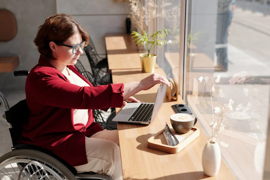 Woman in wheelchair using laptop in a cafe