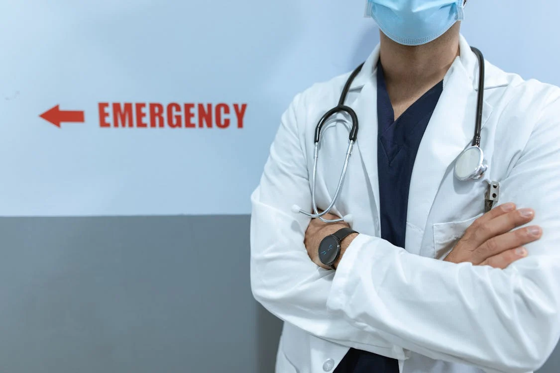 doctor with arms crossed in front of emergency sign