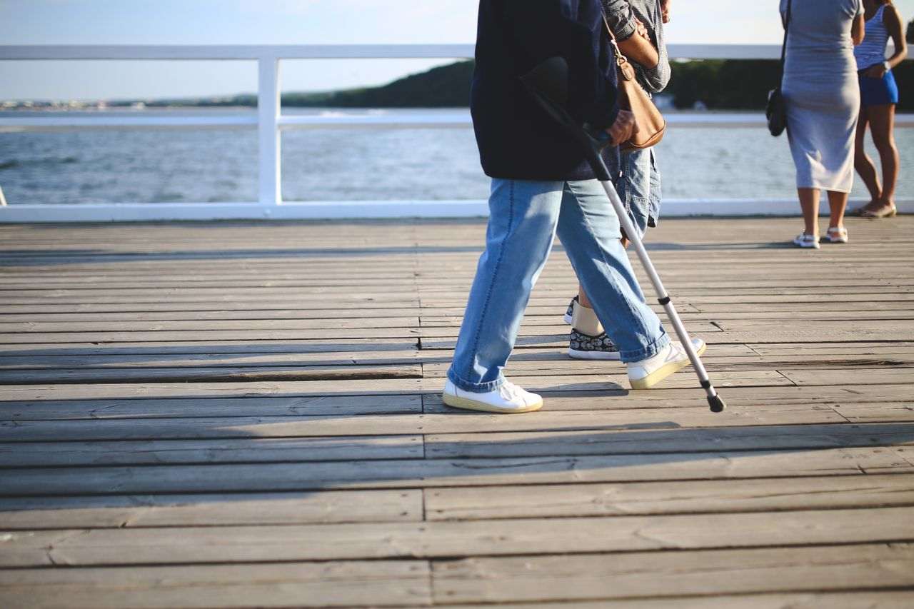 A woman walking with a crutch on a boardwalk