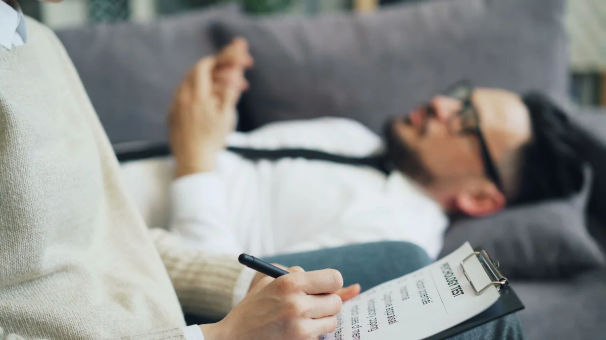 A man with glasses lying on a sofa in a psychology test session