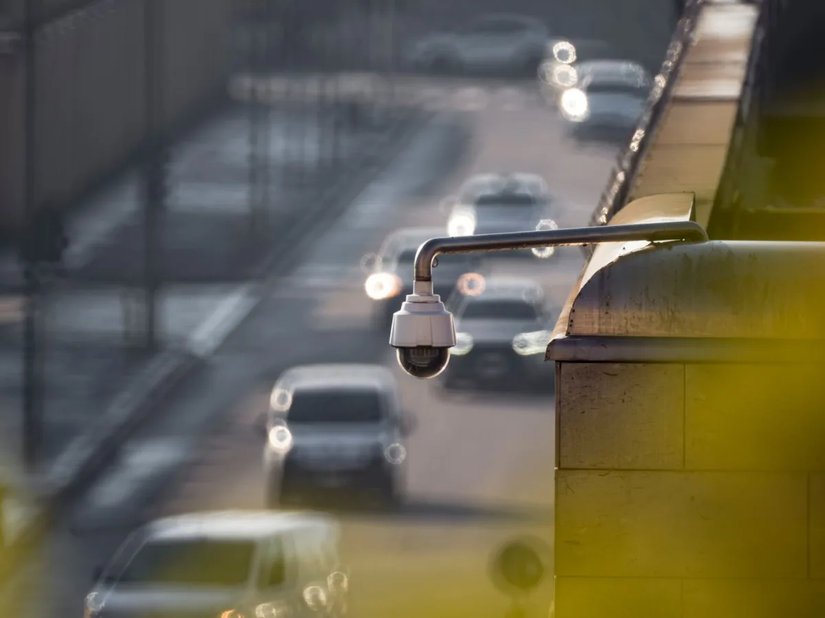 Close up of a security camera overlooking a busy street with cars in the background