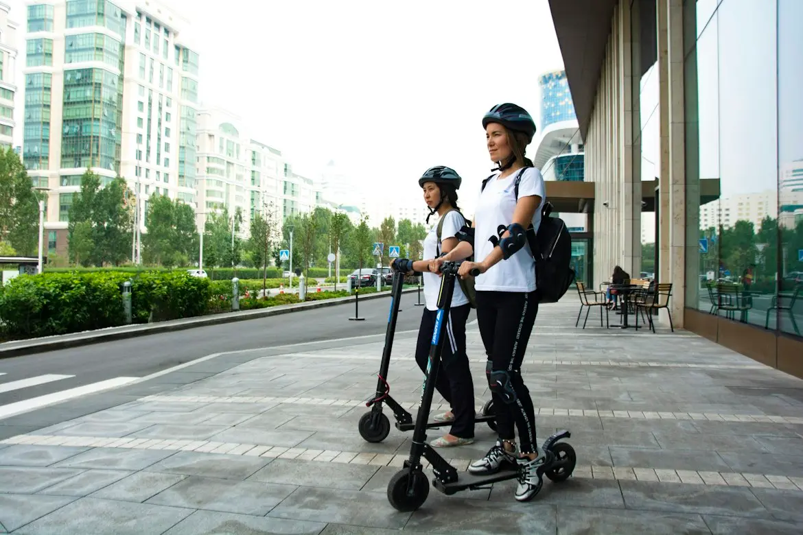 Two riders wearing helmets standing with electric scooters on a city sidewalk